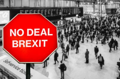 No Deal Brexit written on octagon stop sign with high perspective view defocused passengers at British train station terminal No Deal Brexit written on octagon stop sign with high perspective view defocused passengers at British train station terminal