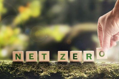 Net zero 2050 Carbon neutral. Net zero greenhouse gas emissions target. Climate neutral long strategy. No toxic gases. Hand puts wooden cubes with netzero icon in green background copy space. Net zero 2050 Carbon neutral. Net zero greenhouse gas emissions target. Climate neutral long strategy. No toxic gases. Hand puts wooden cubes with netzero icon in green background copy space.