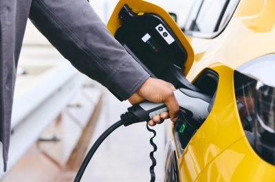 Hand Plugging In Electric Car Outside Office In Car Park Charging Hand Plugging In Electric Car Outside Office In Car Park Charging