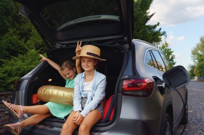 Cute little sisters sitting in trunk while waiting for charging car before travelling on summer holiday. Cute little sisters sitting in trunk while waiting for charging car before travelling on summer holiday.