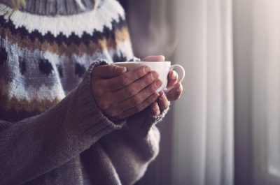 Woman in knitted sweater hands holding cup of warm coffee Woman in knitted sweater hands holding cup of warm coffee