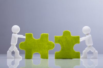 Two Miniature Human Figures Solving Green Jigsaw Puzzles Two Miniature Human Figures Solving Green Jigsaw Puzzles
